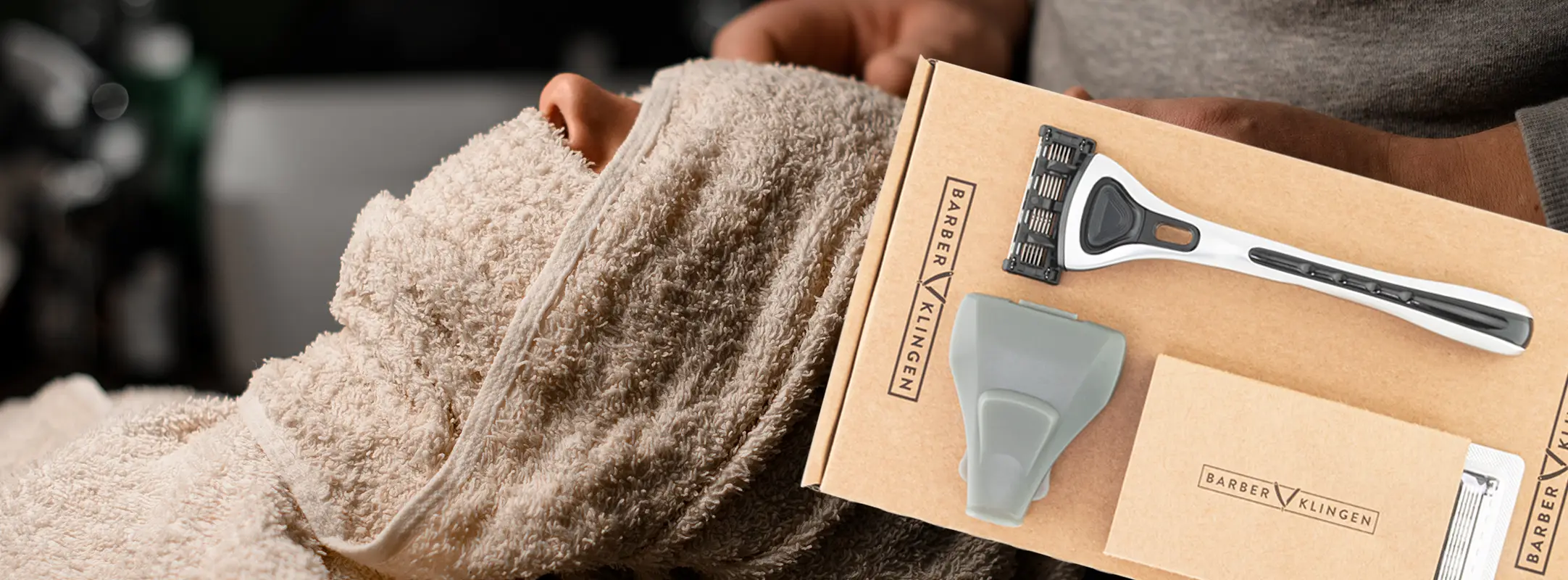 Scheermes abonnement van Barberklingen met scheerset met mesjes en iemand dit in een stoel ligt met een handdoek om zijn hoofd om te koelen voor of na het scheren.