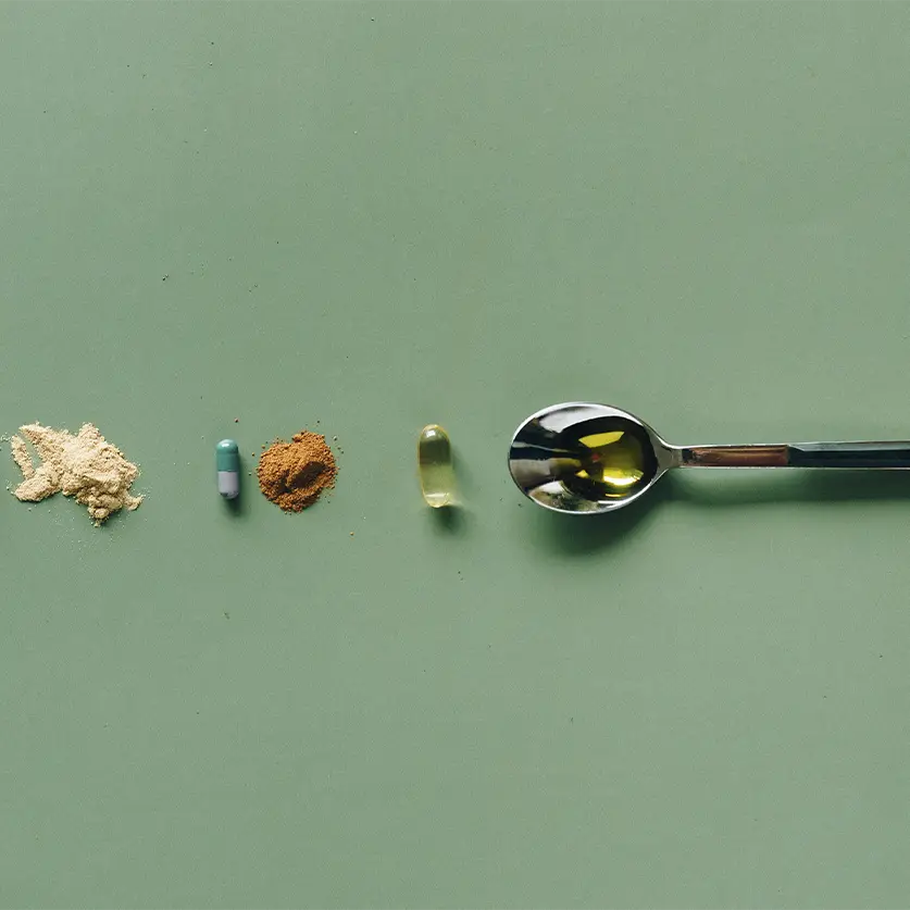 Vitamines en supplementen op een groen kleed met een lepel olijfolie