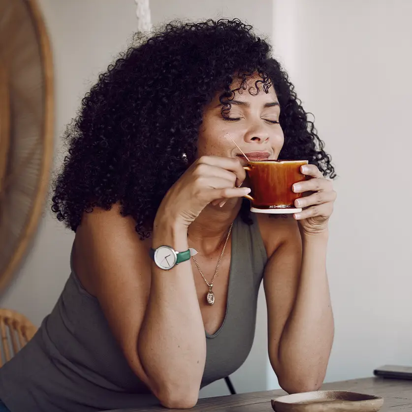 Vrouw die geniet van een vers gezet bakje koffie uit haar koffiemachine abonnement, zittend aan tafel.