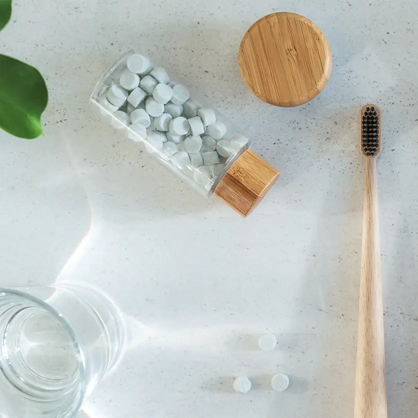 Tandpasta tabs in een doorzichtig potje met bamboe tandeborstel op een marmeren badmeubel.