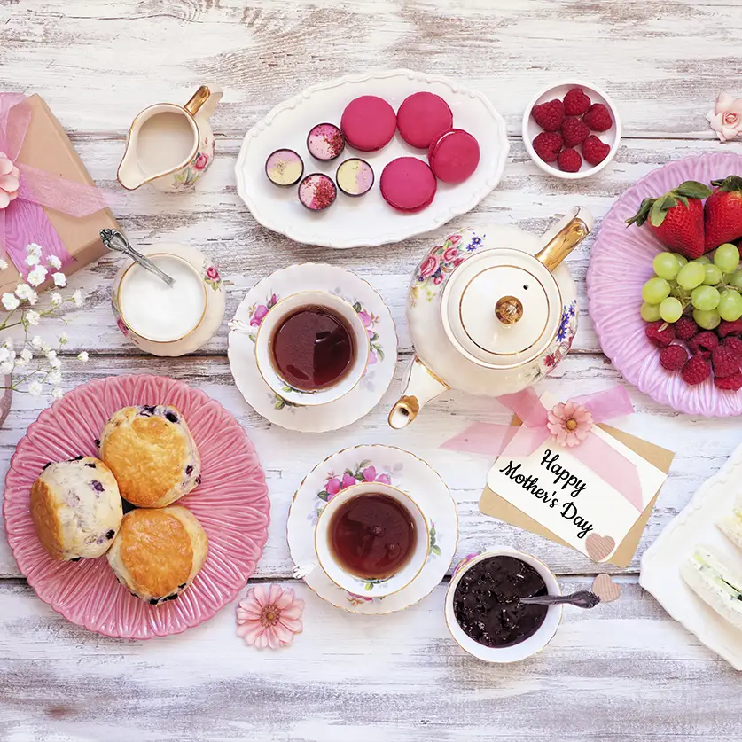 Een tafel met thee, scones, druiven, marmelade en andere zoete lekkernijen die ook als theepakket cadeau zijn te geven.