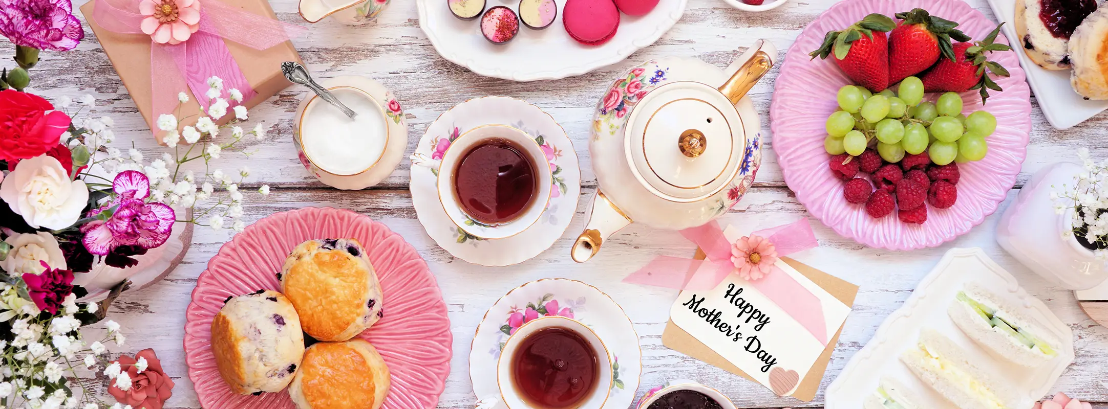 Een tafel met thee, scones, druiven, marmelade en andere zoete lekkernijen die ook als theepakket cadeau zijn te geven.