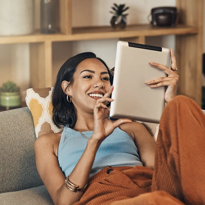 Blije vrouw die op de bank een ebook ligt te lezen op haar tablet
