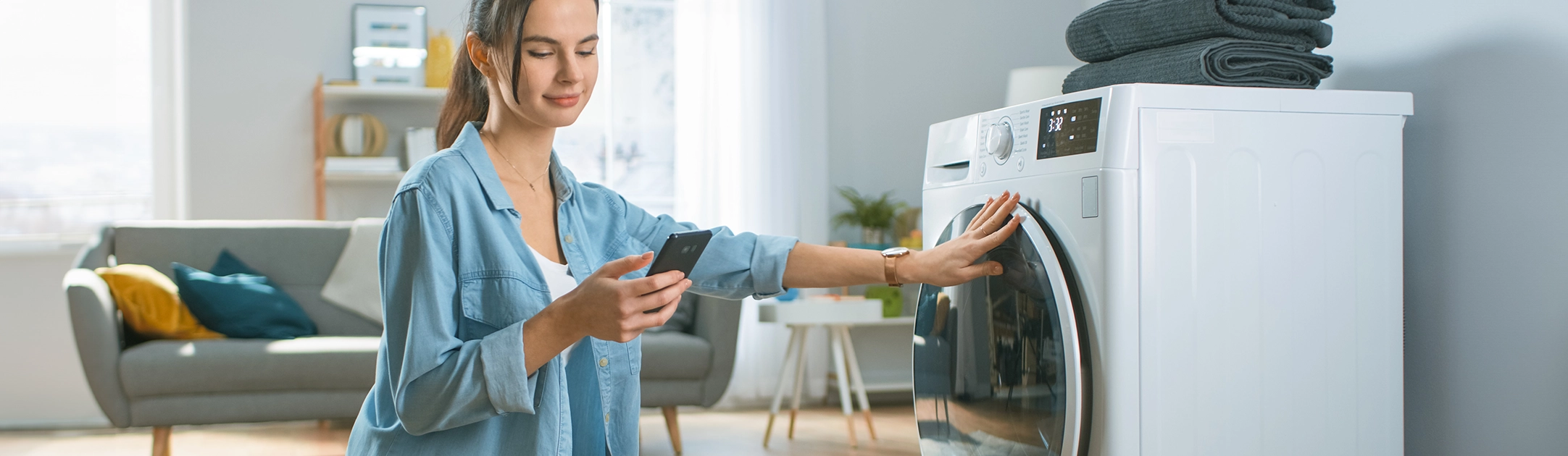 Vrouw bij een wasmachine met een smartphone in haar hand