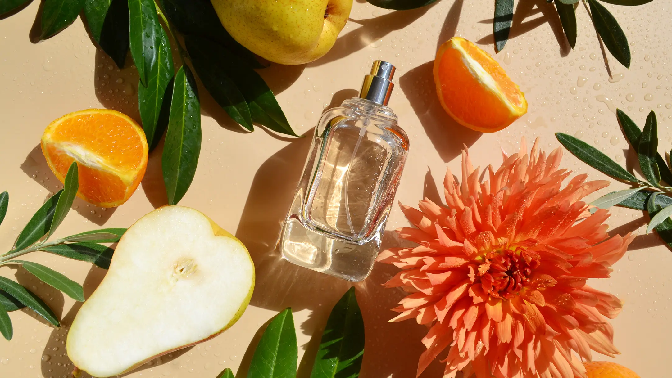 Een parfumflesje op de grond met peren, sinaasappels, bloemen en bladeren