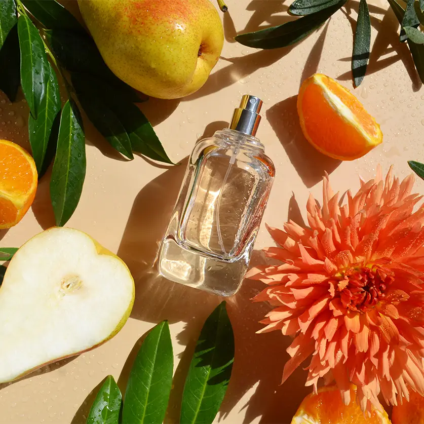 Een parfumflesje op de grond met peren, sinaasappels, bloemen en bladeren